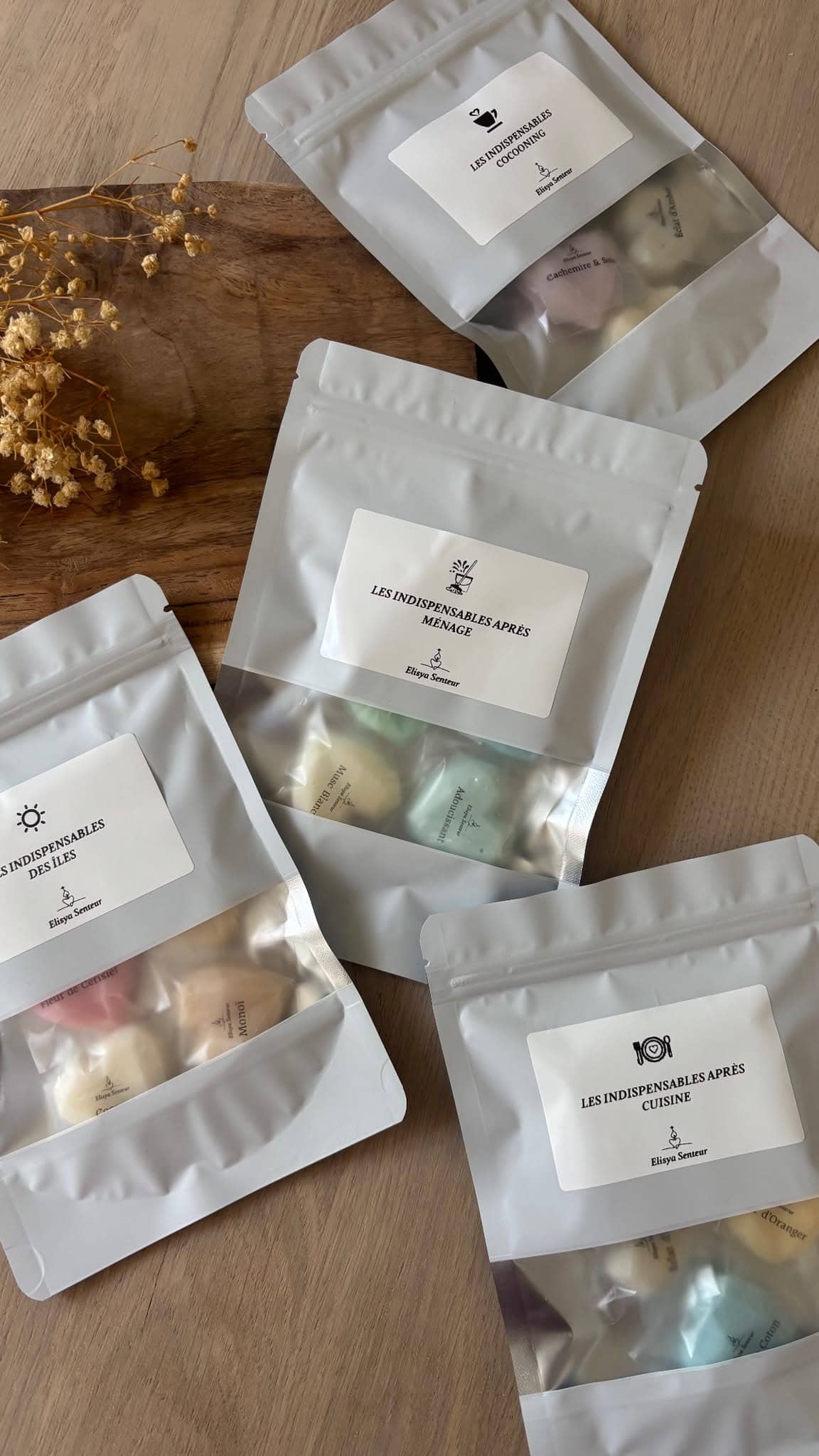 Quatre sachets blancs Elysia Senteur Les Indispensables — Cocooning, Après Ménage, Des Îles, Après Cuisine — posés sur surface bois avec fleurs séchées. — vue 1