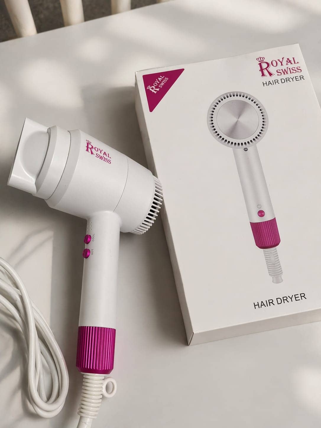 Sèche-cheveux blanc et fuchsia de marque Royal Swiss posé à côté de sa boîte sur une surface blanche. — vue 1